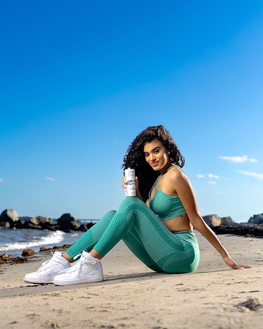 Vagari on the coast: a woman in green activewear holding the light-colored can by the ocean